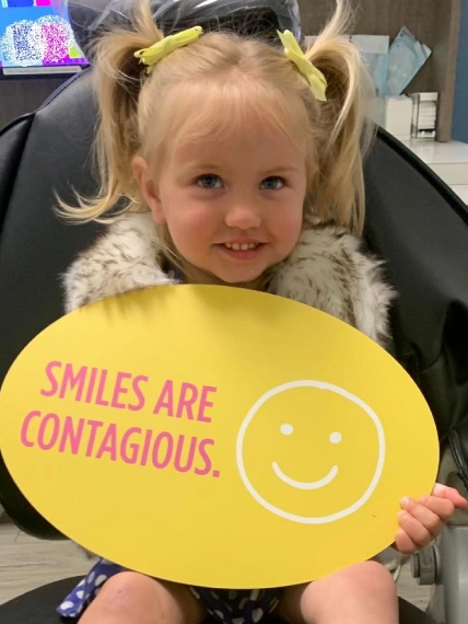 Happy young girl patient at Edna dentistry. The girl is taking a photo with the doctor holding in hand a card on which is written: "We love our patients".